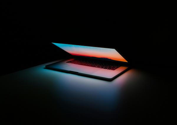 a laptop half closed with a colorful screen and keyboard in a dark room.