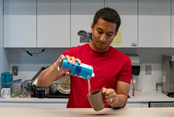 Man pouring sugar into a ceramic coffee mug in a workplace kitchen