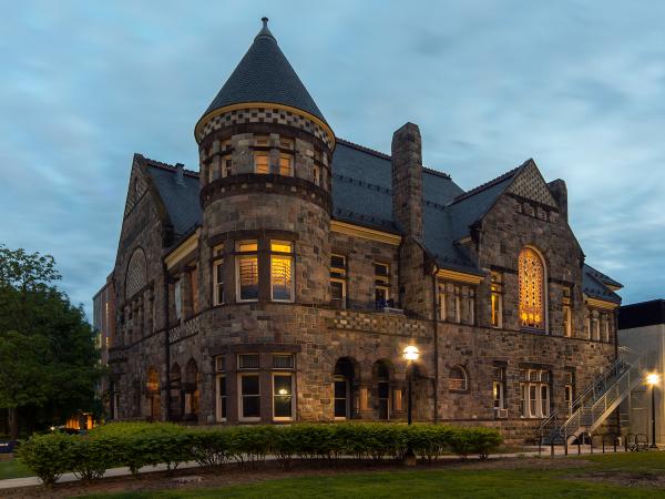 View of Newberry Hall, a Richardsonian Romanesque building constructed of multicolored bricks, at dusk.
