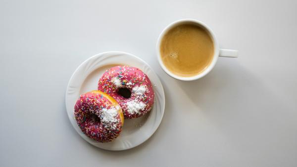 Two donuts on plate next to coffee