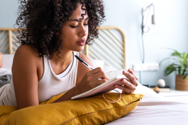 Woman lying in bed with a journal and pen in her hand.