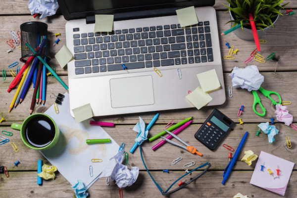 Photo from above of a laptop, with pencils, pens and sticky notes scattered around messily.