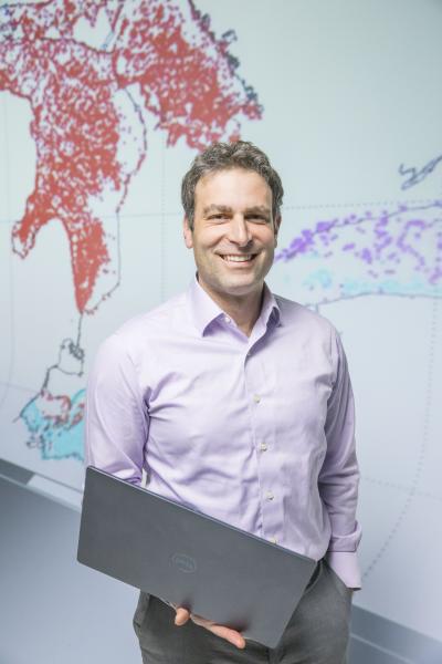 Photo of Dr. Hoffman holding a laptop in front of a map of the Great Lakes made of data points