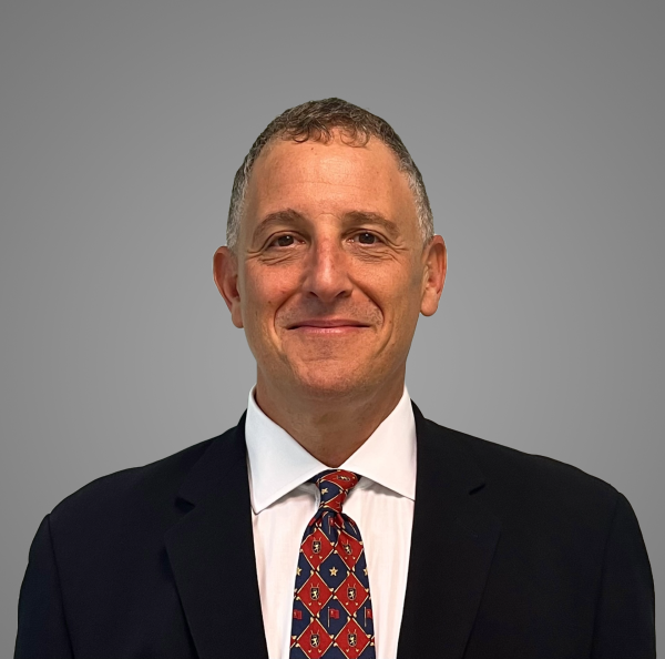Headshot of Dr. Brian Becker; he's wearing a dark suit, white shirt and red tie and a closed mouth smile.  He has short curly brown hair and a fair complexion.