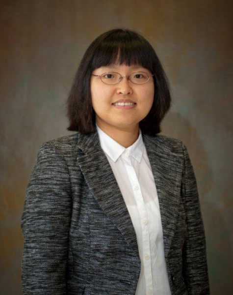 Headshot of person in grey suit with glasses and brown background