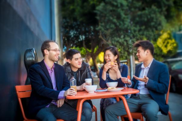 Four people at a table outdoors drinking coffee and laughing