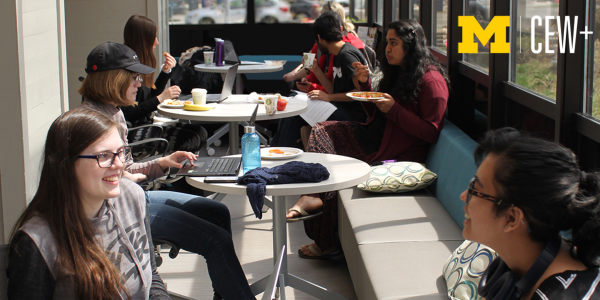 Group of people sitting at tables and benches enjoying food and conversation in a bright indoor space.