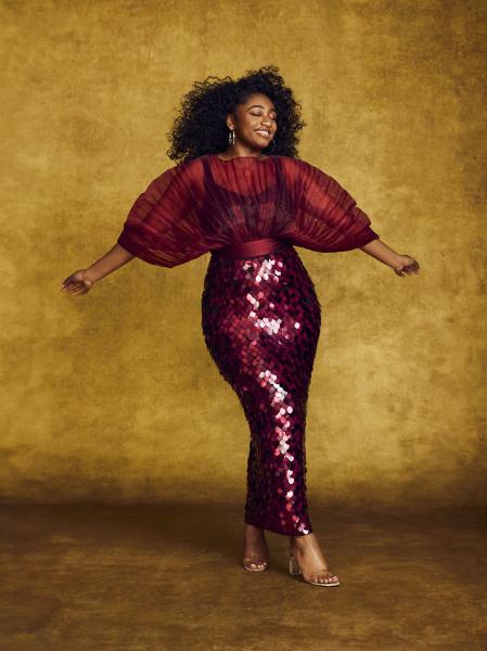 Woman in dark red sparkly dress with arms held out