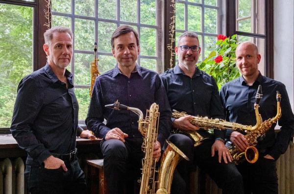 Group portrait of four people, each with a saxophone, and all wearing black.