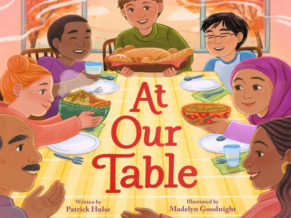 The cover of the picture book “At Our Table,” showing a multicultural group of adults and children sitting around a dining table holding bowls of food.