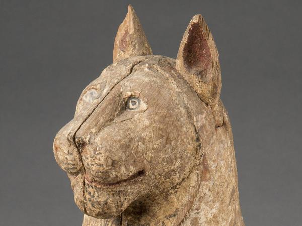 Close-up of the head of a wooden cat coffin with a split down the middle, showing where it separates into two pieces. Black, white, and red paint emphasize the cats facial features.