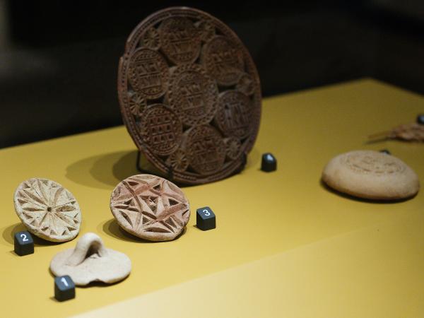 Display case showing, from left to right, three small bread stamps with Christian iconography, a much larger stamp with detailed Christian symbols carved into its surface, and a stamped piece of Eucharistic bread.