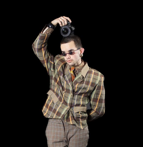 Image depicts artist William Hohe on a black backdrop holding a camera on their head.