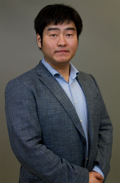 Dr. Tiantian Yang facing the camera at a 45 degree angle with hands clasped, wearing blazer with a light blue collared shirt with a neutral light brown background.