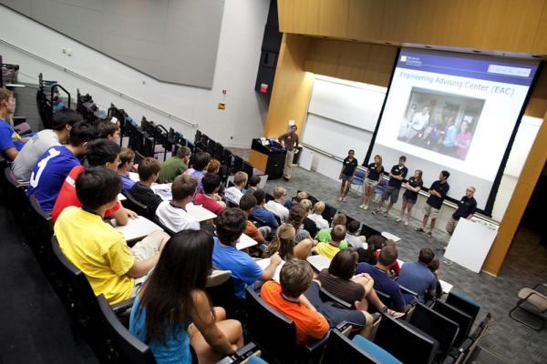 Panel presentation by the Engineering Advising Center (EAC) at the U-M College of Engineering. Students seated in theater style seating lecture hall listening to a panel of seven speakers standing at the front of the room.
