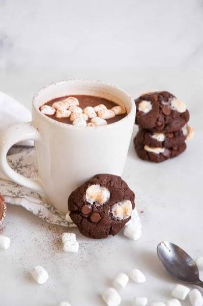 A ceramic mug filled with hot cocoa topped with mini marshmallows next to chocolate marshmallow cookies.