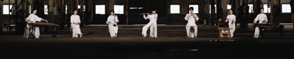 Ensemble PHASE musicians perform traditional Korean music in a spacious, dimly lit industrial setting, playing traditional Korean instruments while dressed in white.