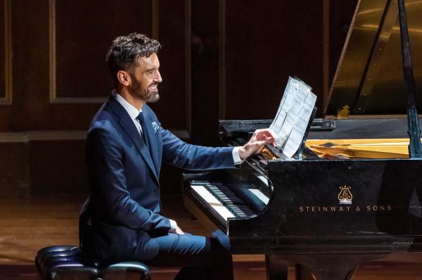 Cameron Stowe on stage seated at a piano.