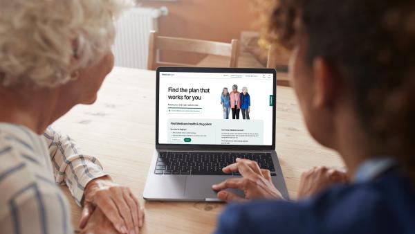 Two women looking at a laptop with the Medicare website displayed
