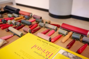 Printmaking equipment - brayers and rollers - is arranged next to a yellow Bristol pad of paper.
