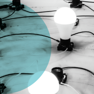 Several light bulbs connected by black wires sit on a wooden tabletop. One bulb shines brightly, while a transparent blue circle overlays part of the scene.