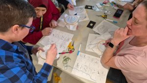 several people gathered around a table take part in a Stamps Gallery embroidery workshop.
