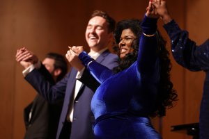 Performers stand holding hands for a bow on stage.