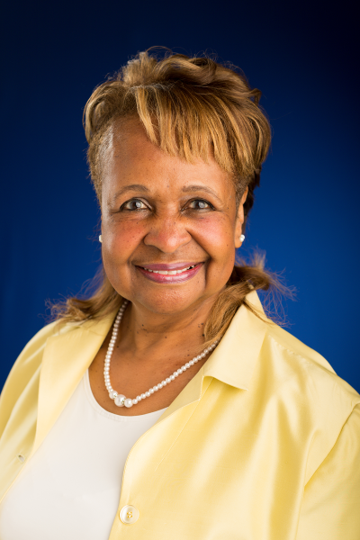 Wendy Woods - older African American woman with short blonde hair, smiling, wearing yellow collared shirt, white necklace, and white shirt underneath.