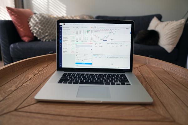 laptop with a stock tracker on the screen ⏤ the laptop is on a brown round table and there's a couch in the background