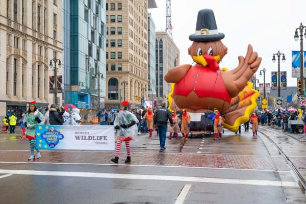 Woodward Avenue shot of volunteers pulling the turkey balloon, surrounded by parade crowds lining the sidewalk.